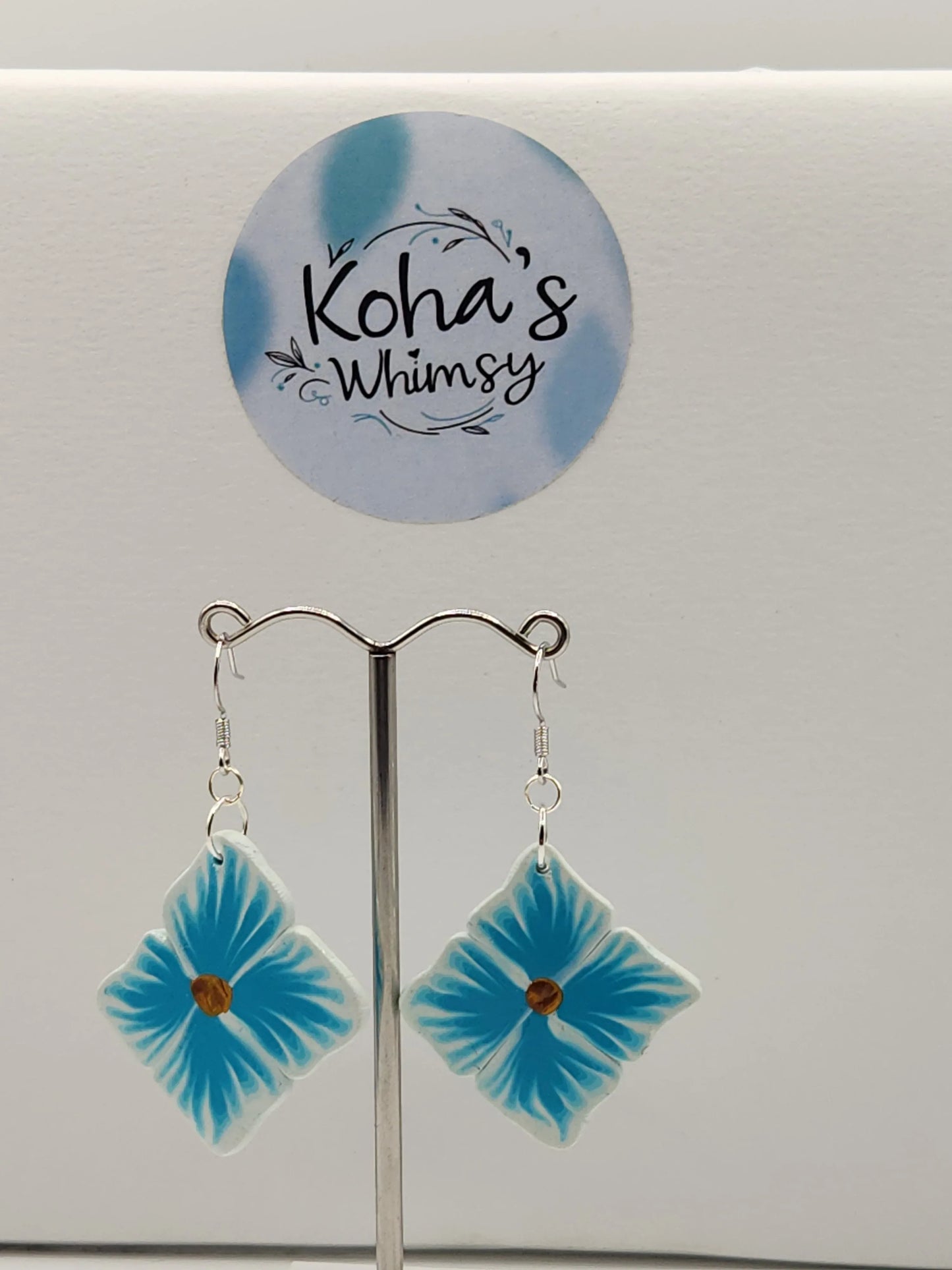 Blue floral dangle earrings from Koha's Whimsy on a silver display stand.