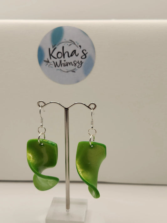 Green dangle earrings by Koha's Whimsy displayed on a metal stand with a twisted design.