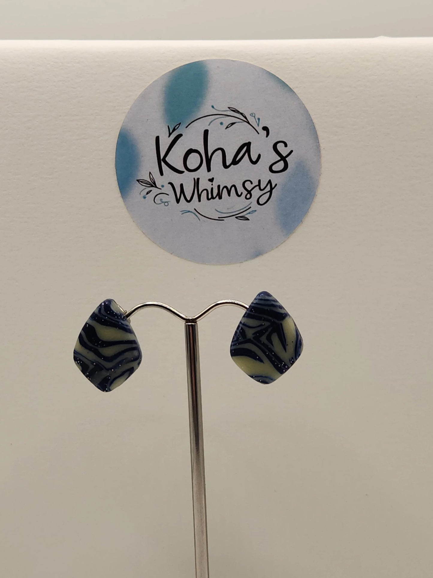 Blue and ivory earrings with flecks of sparkle by Koha's Whimsy on a jewelry stand.