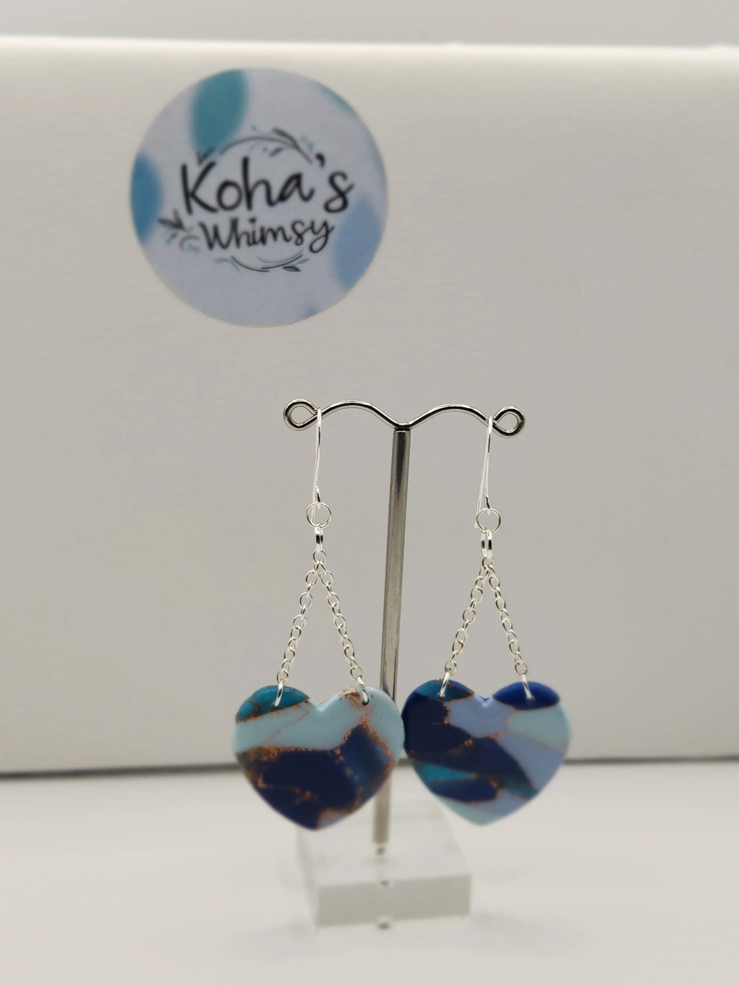 Blue heart dangle earrings by Koha's Whimsy, with copper-colored marbling and silver-colored chains.