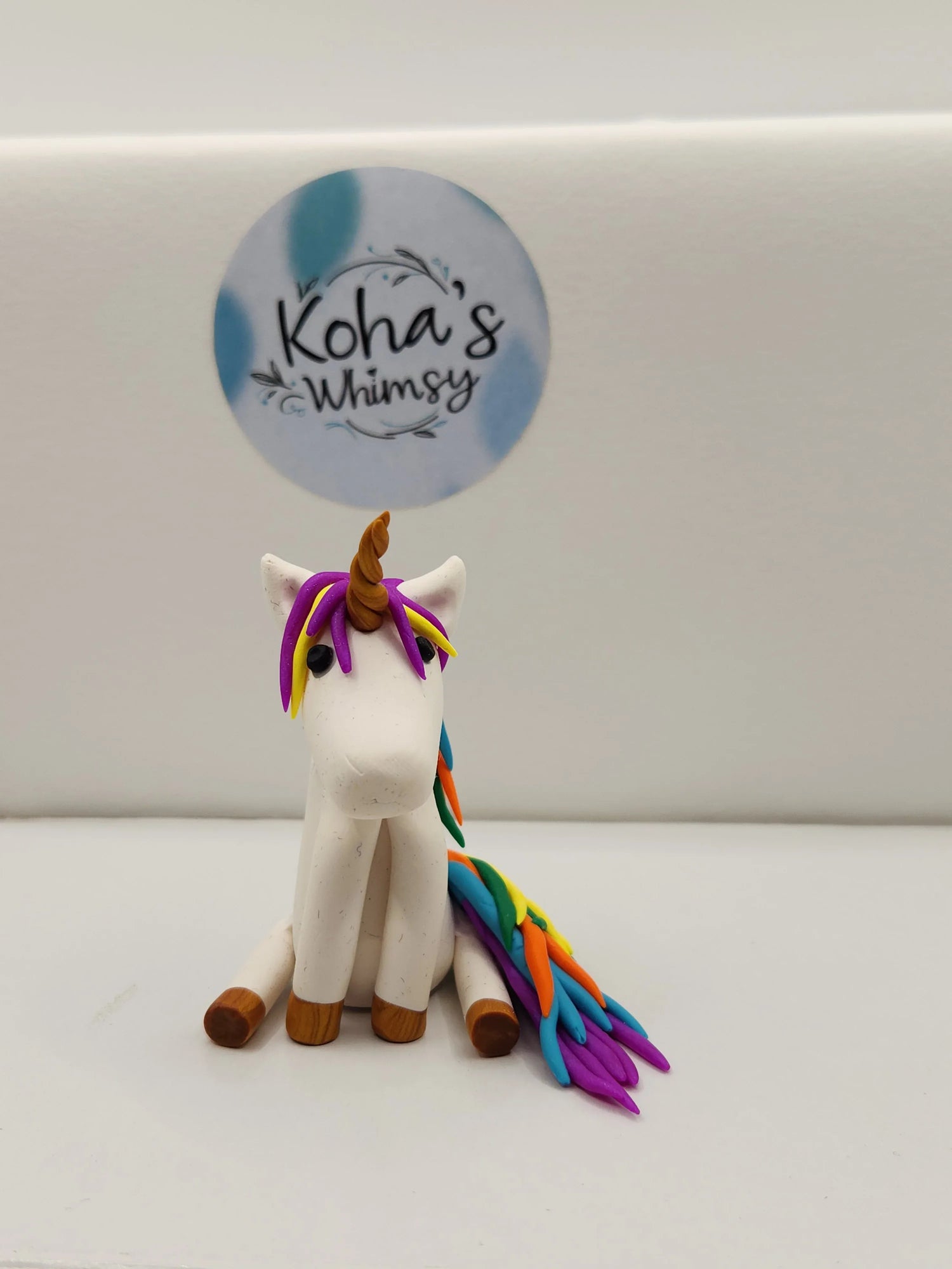 White clay unicorn figurine by Koha's Whimsy with colorful rainbow mane and tail and a light brown horn.