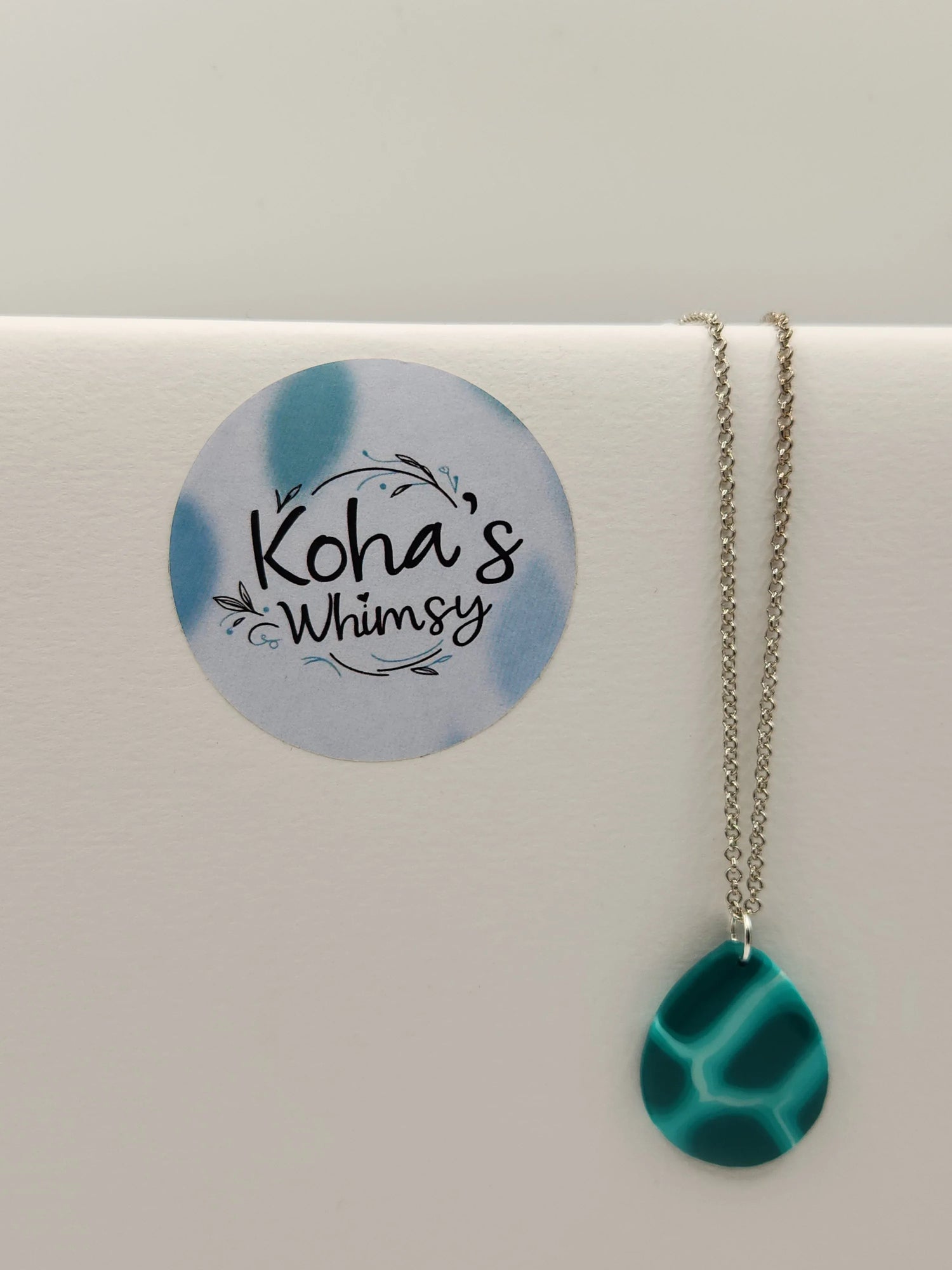 Teal teardrop pendant necklace by Koha's Whimsy with a turtle shell pattern, hanging from a silver chain.