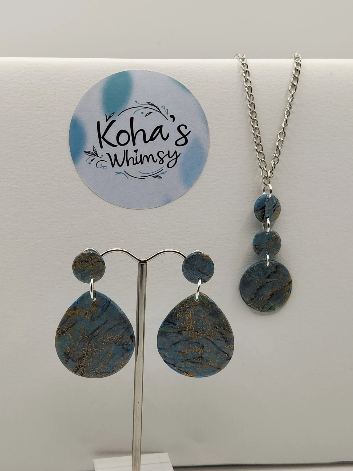Blue clay jewellery set by Koha's Whimsy, including earrings and pendant, with gold flecks and silver chain.