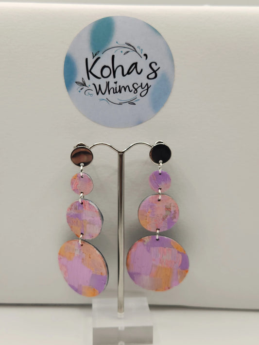 Pastel watercolour circular dangle stud earrings from Koha's Whimsy, displayed on a stand with a circular logo in the background.