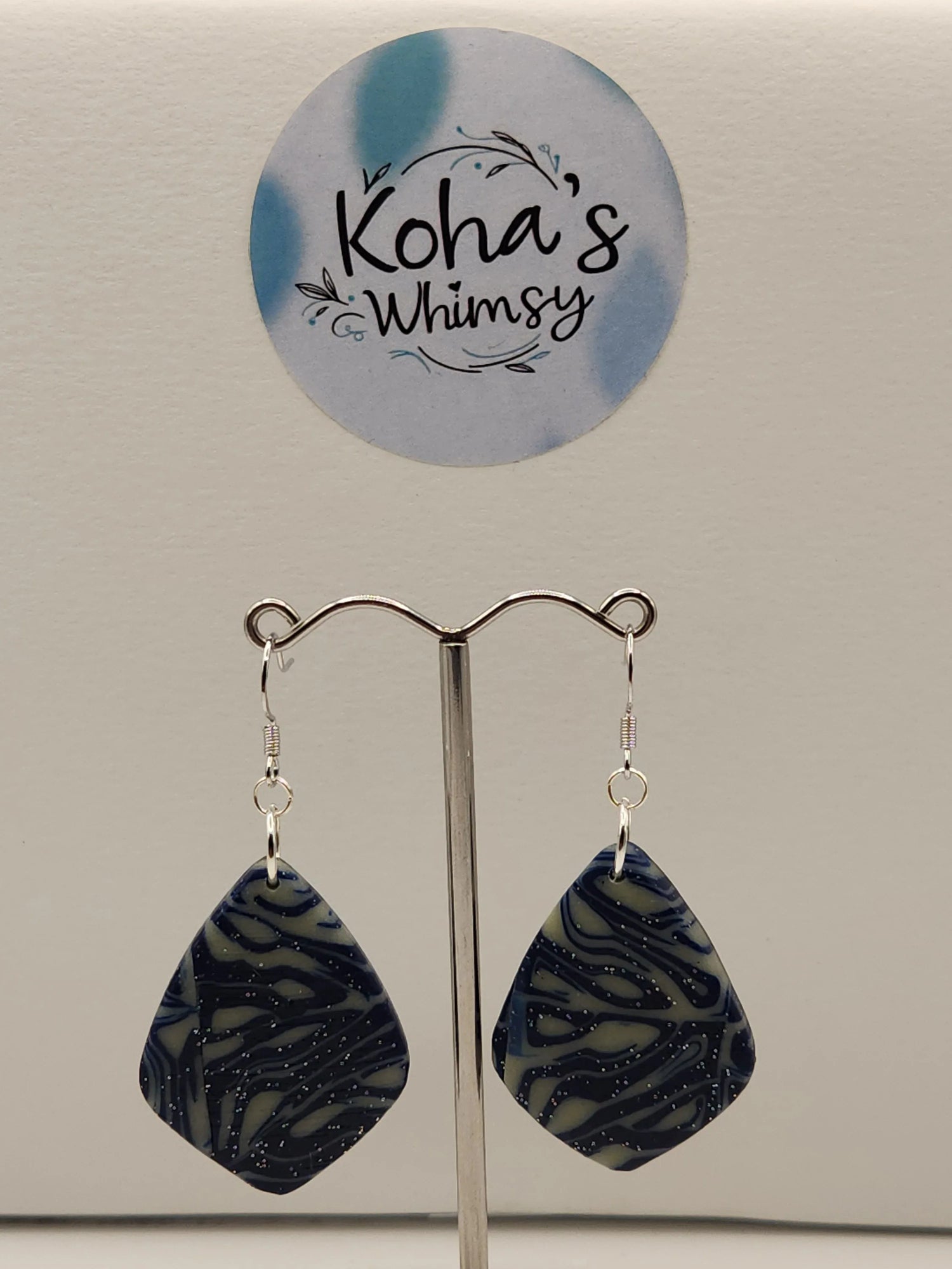 Diamond dangle earrings with a swirled pattern and subtle shimmer, by Koha's Whimsy, displayed on a silver-toned jewelry stand.