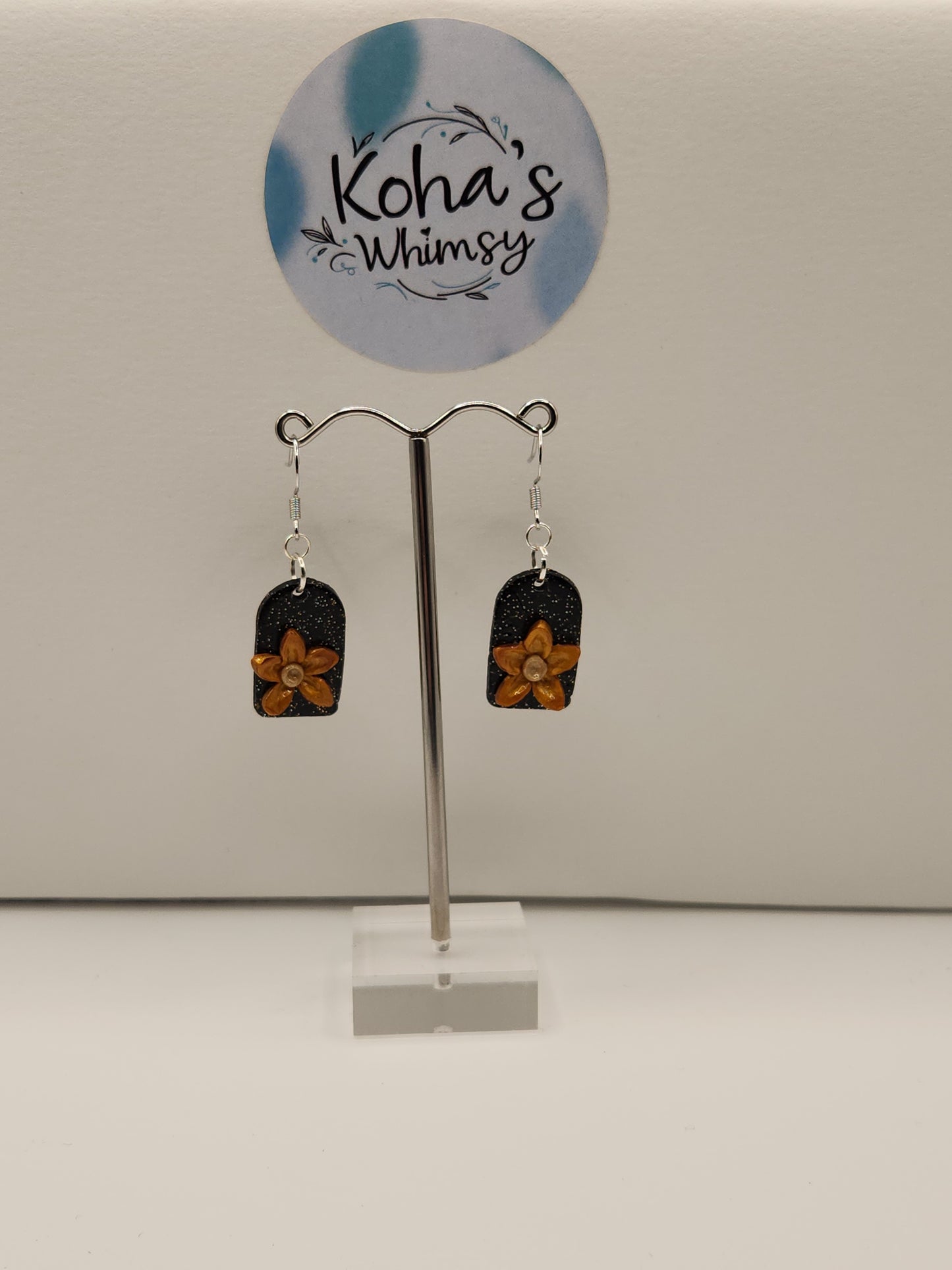 Golden bloom dangle earrings displayed showing elegant floral design with golden flowers against black glittery arch"