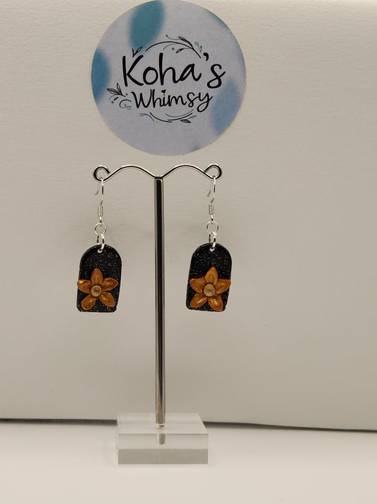 Handmade polymer clay dangle earrings with delicate golden flowers on glittery black arch background