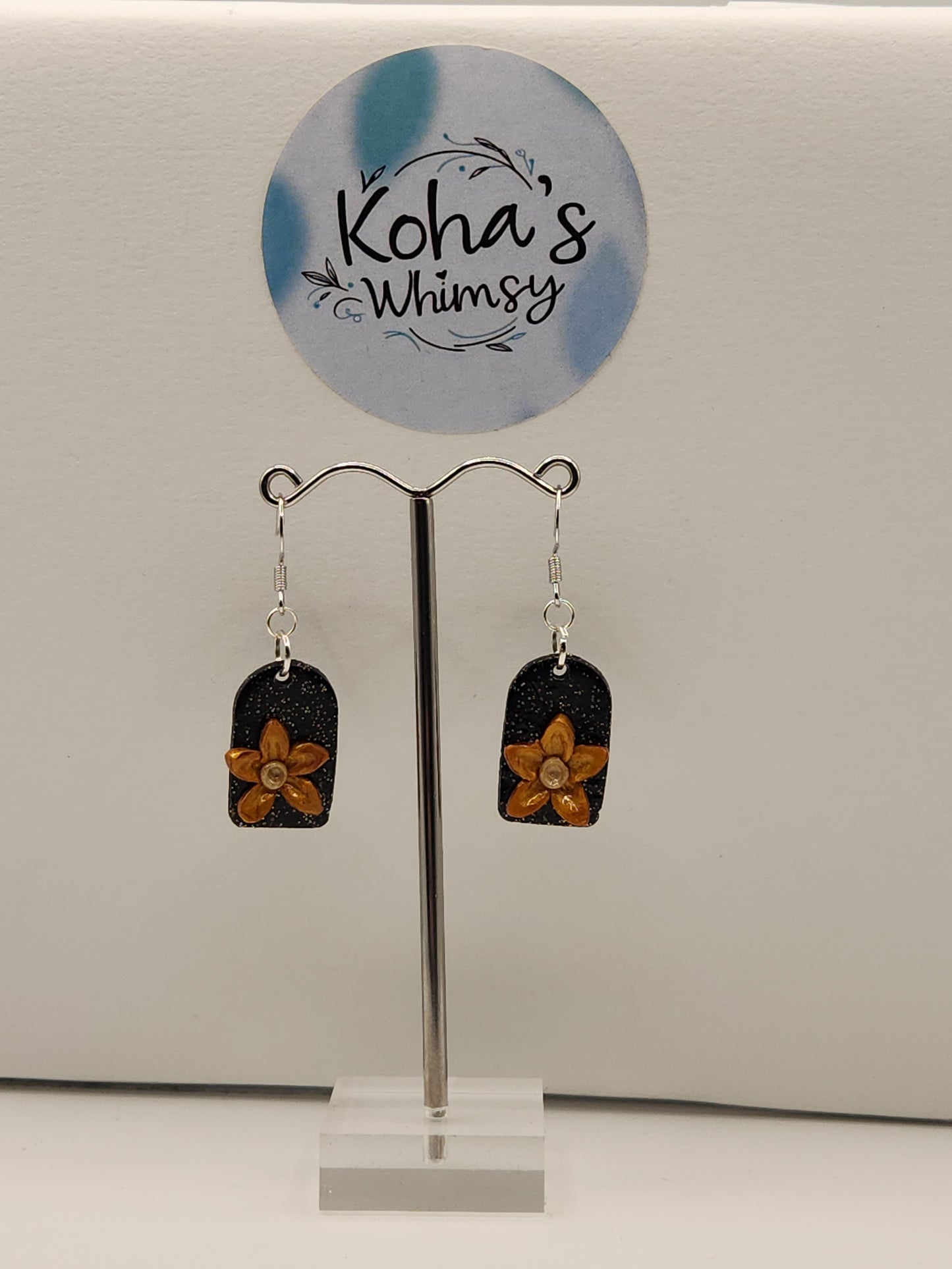 Close-up of golden bloom earrings showing hand-sculpted golden flowers with subtle shimmer on black glitter