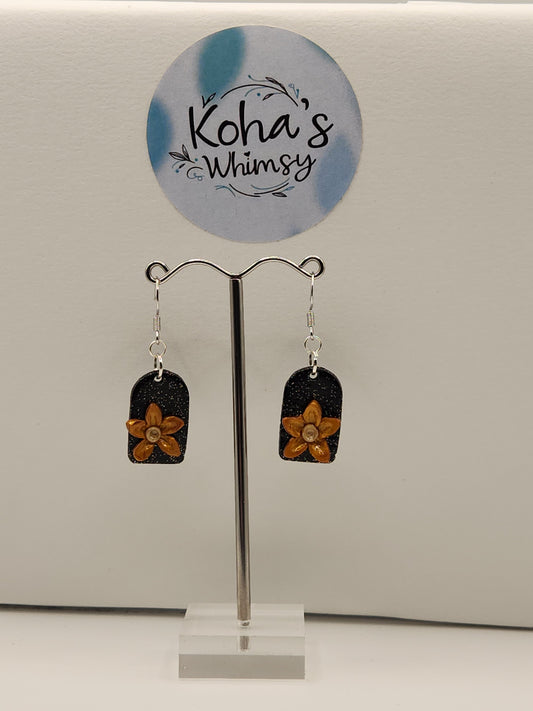 Close-up of golden bloom earrings showing hand-sculpted golden flowers with subtle shimmer on black glitter