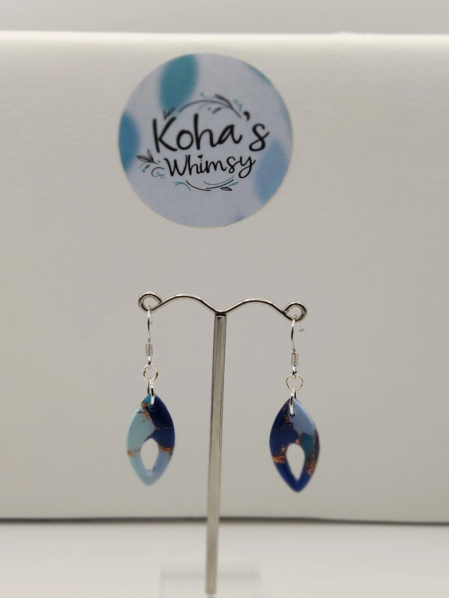 Dangle earrings with a pointed ellipse shape from Koha’s Whimsy, featuring light and dark blue marbled patterns with copper accents.