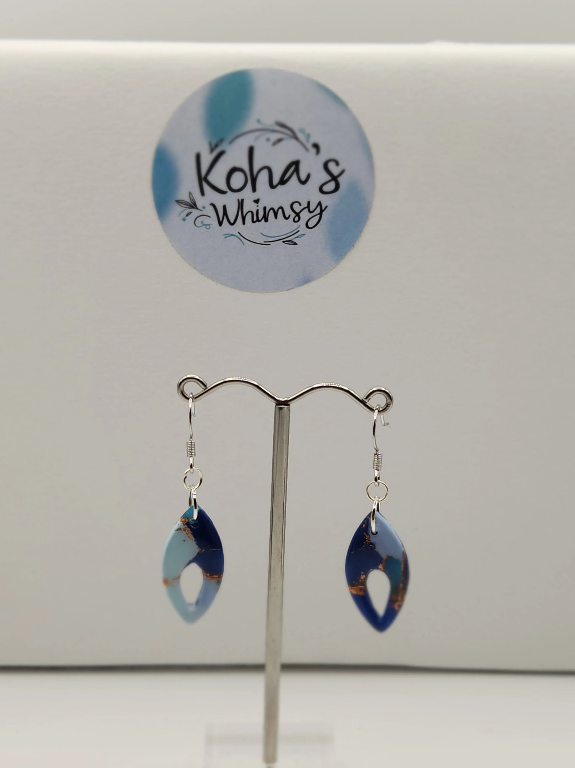 Dangle earrings with a pointed ellipse shape from Koha’s Whimsy, featuring light and dark blue marbled patterns with copper accents.